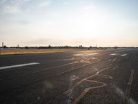 a runway in the sunlight with a person sitting on the ground near an airplane taking off