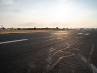 a runway in the sunlight with a person sitting on the ground near an airplane taking off