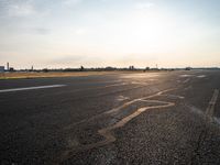 a runway in the sunlight with a person sitting on the ground near an airplane taking off