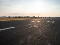 a runway in the sunlight with a person sitting on the ground near an airplane taking off