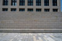 a sidewalk has many square stones arranged around it to create a pattern on it, a building in the background