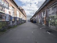 a blurry photo of an empty street with dump cans in between two buildings and trees