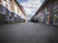 a blurry photo of an empty street with dump cans in between two buildings and trees