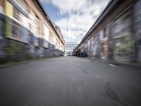 a blurry photo of an empty street with dump cans in between two buildings and trees