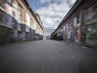 a blurry photo of an empty street with dump cans in between two buildings and trees