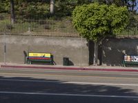 two park benches sit next to each other on the side of the street against a concrete wall