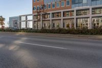 the road with no vehicles is empty in front of a city building with tall glass windows