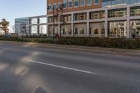 the road with no vehicles is empty in front of a city building with tall glass windows