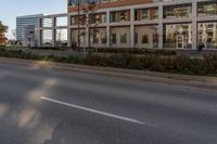 the road with no vehicles is empty in front of a city building with tall glass windows