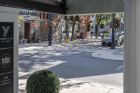 a man is walking down the street, passing by some bushes and a traffic light