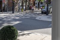 a man is walking down the street, passing by some bushes and a traffic light