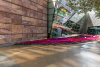 the building has many colored flowers in front of it with a reflection of a glass building in the middle of the building