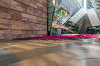 the building has many colored flowers in front of it with a reflection of a glass building in the middle of the building