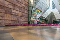 the building has many colored flowers in front of it with a reflection of a glass building in the middle of the building