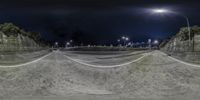 a skate park at night with a bike ramp to the right and lights on in the distance