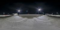 a skate park at night with lights on and empty ramps on either side of it