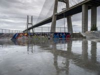 this is an urban skate park with graffiti painted on it's concrete ground and a bridge in the background