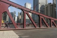 the red steel bridge crosses the street between tall buildings and buildings across the street and in a city with high buildings