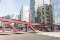 the red steel bridge crosses the street between tall buildings and buildings across the street and in a city with high buildings