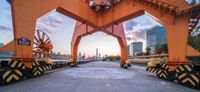 two orange steel lifting lifts hold a bridge with city buildings in the background with an old steel