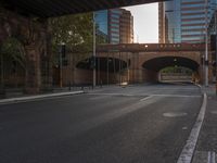 the empty city street in front of skyscrapers and road crossing under a bridge with trees