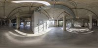 a room with columns and ceilings and arches covered by light reflecting off the windows on the concrete floor