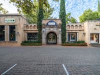 the entrance to an old style marketplace store on the corner of a sidewalk surrounded by trees