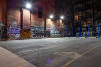 a empty parking lot with graffiti on the walls at night in an old factory complex