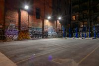 a empty parking lot with graffiti on the walls at night in an old factory complex