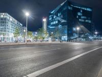 the empty roadway is lined with modern building facades, lights, and empty streets during the night