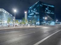 the empty roadway is lined with modern building facades, lights, and empty streets during the night