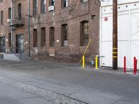 a street with some tall brick buildings in the background, next to a yellow fire hydrant