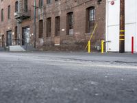 a street with some tall brick buildings in the background, next to a yellow fire hydrant