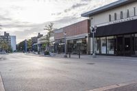 a paved street with businesses along side in urban area under a cloudy sky, as seen from across the street