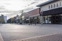 a paved street with businesses along side in urban area under a cloudy sky, as seen from across the street