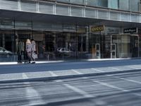 a person walking down a sidewalk in front of a building with a storefront and car in the background