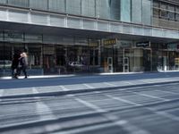 a person walking down a sidewalk in front of a building with a storefront and car in the background