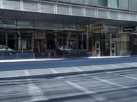 a person walking down a sidewalk in front of a building with a storefront and car in the background