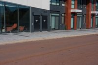 there are two wooden chairs near the street corner of this city street building, and a red brick sidewalk to the right