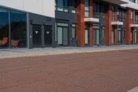 there are two wooden chairs near the street corner of this city street building, and a red brick sidewalk to the right