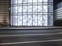 a building has a glass front in a city street, with greenery in front