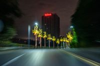 a street with some palm trees and some buildings at night time in the background is blurred