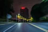 a street with some palm trees and some buildings at night time in the background is blurred