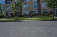 a road near a tall building with lots of windows and trees and plants in front