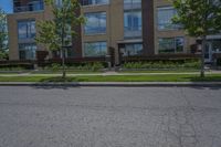 a road near a tall building with lots of windows and trees and plants in front