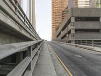 the car is traveling along the empty road by the large city buildings in the distance