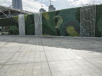 a tiled walkway near an ivy wall and large building behind it at the city park