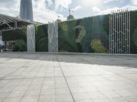 a tiled walkway near an ivy wall and large building behind it at the city park