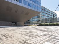 a building with many windows next to a sidewalk with a stone block pattern on the outside