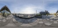 a 360 - view lens of a street scene with multiple buildings on both sides and cars parked in the distance